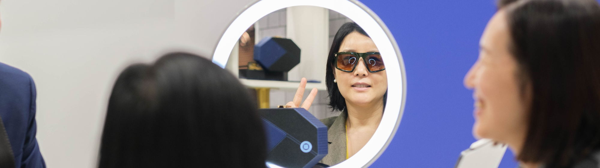 Une femme avec des lunettes de soleil souriant à travers un miroir à SILMO Paris